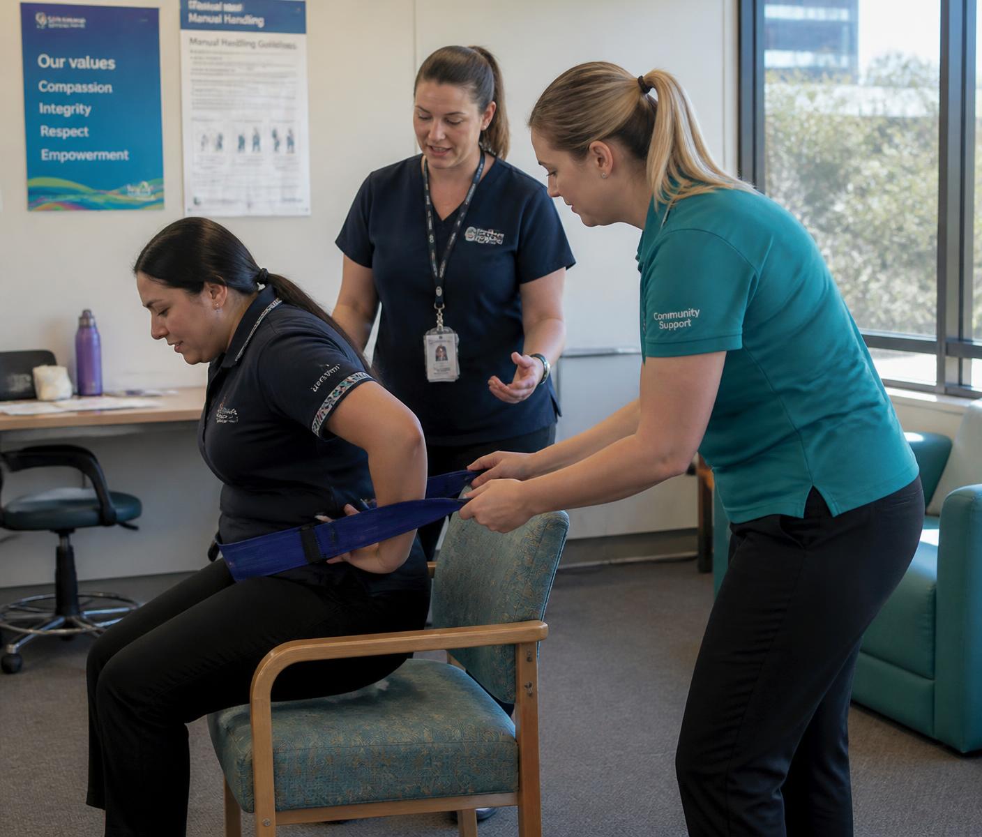 A registered nurse trainer guiding two community support workers through a safe transfer technique at their workplace